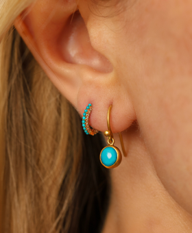 Close-up of a woman's ear showcasing two elegant earrings: a gold hoop adorned with small turquoise stones and a gold drop earring featuring a turquoise gemstone.
