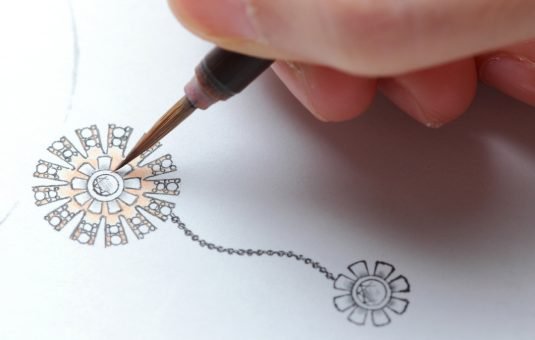 A hand holding a fine-tipped pen is drawing intricate floral designs on white paper, showcasing the art of illustration and creativity.