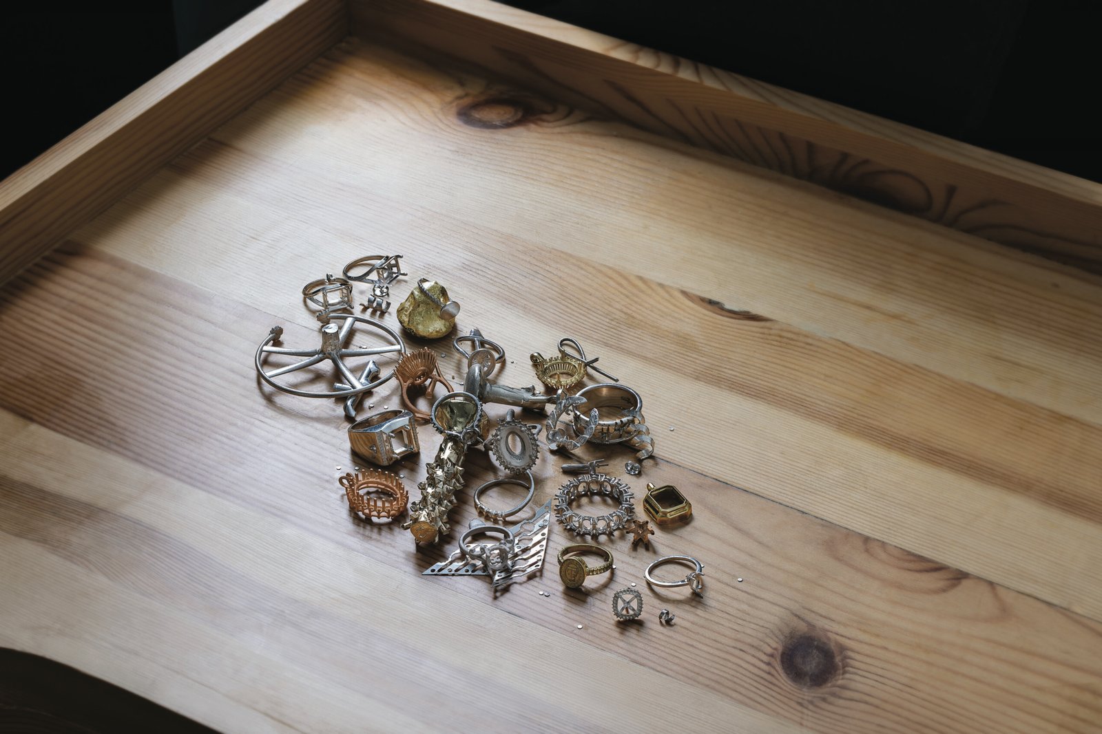 Assorted jewelry pieces including rings, pendants, and brooches displayed on a wooden tray, showcasing a variety of metals and designs.