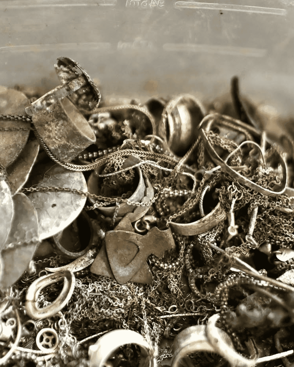 A close-up image of a collection of assorted silver jewelry, including rings, chains, and decorative pieces, all piled together in a transparent container.