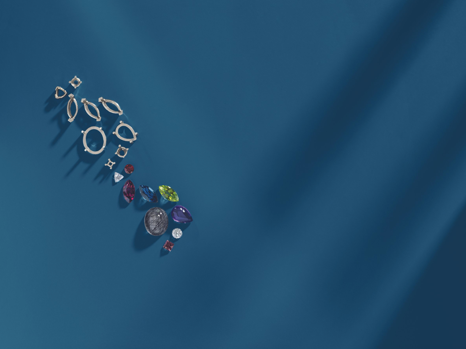 Assorted jewelry pieces including colorful gemstones and silver settings arranged on a deep blue background, showcasing a variety of shapes and styles.