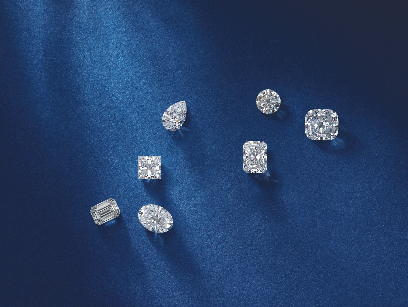 A collection of various diamond cuts including pear, round, princess, cushion, and emerald shapes, displayed on a deep blue background, showcasing their brilliance and clarity.
